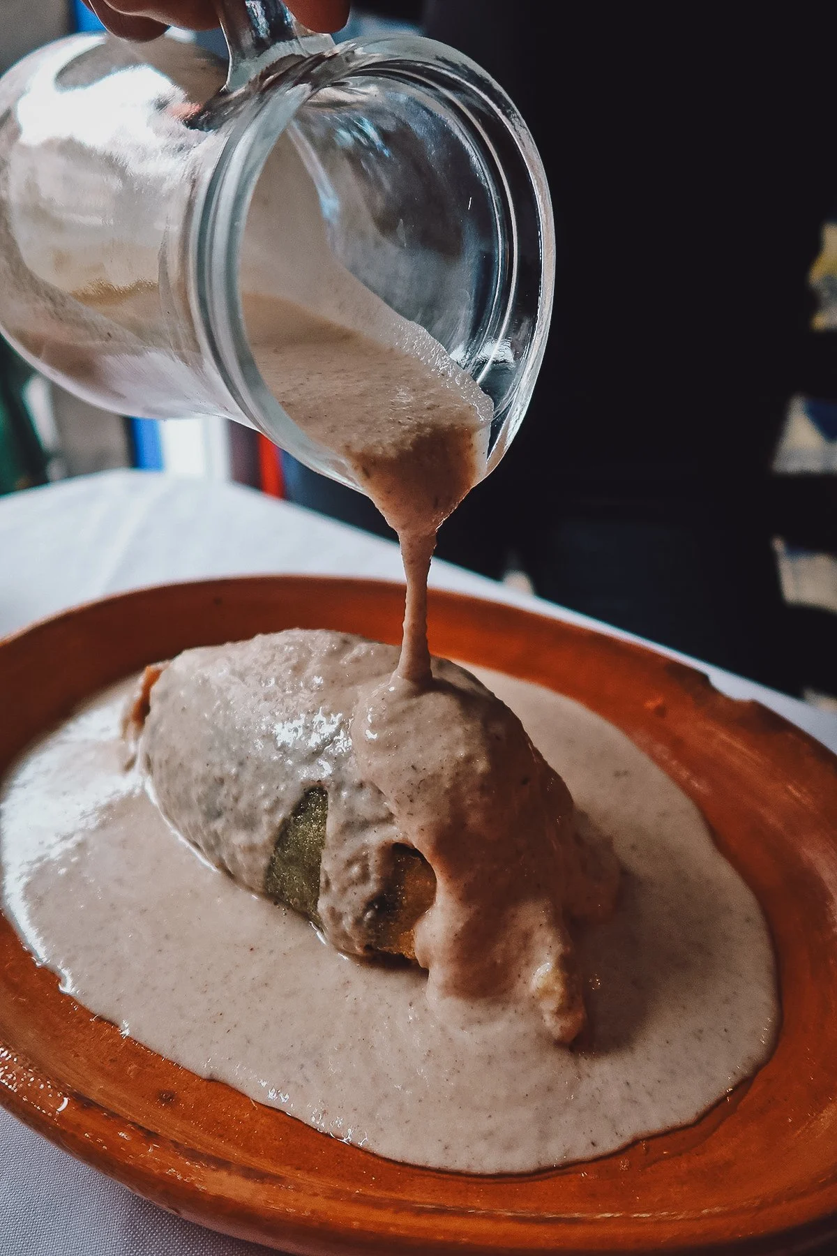 Pouring walnut cream sauce on the stuffed poblano chile